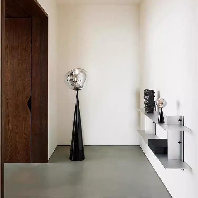 A floor lamp with a reflective, deformed globe design, featuring a black base and custom colored glass, displayed in an interior setting.